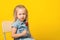 Cute child girl holding lollipop over yellow background. Summer fashion concept. Kids fashion, copy space. Happy girl eats big