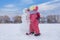 Cute child girl making snowman at bright snowy place. Winter outdoor activities