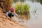 Cute child girl in pink knitted hat plays with stick on river side with sand beach