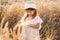 cute child girl in straw hat and beige muslin dress in wheat field on sunset