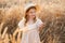 cute child girl in straw hat and beige muslin dress in wheat field on sunset