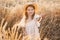 cute child girl in straw hat and beige muslin dress in wheat field on sunset