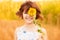 Cute child girl wear dress with sunflower in summer field. Happy little girl hide eye with sunflower. Summer holidays