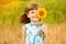 Cute child girl wear dress with sunflower in summer field. Happy little girl hide eye with sunflower. Summer holidays