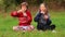 Cute child girls sits on grass with crossed legs and blowing soap bubbles in park. Playing with soap bubbles