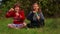 Cute child girls sits on grass with crossed legs and blowing soap bubbles in park. Playing with soap bubbles