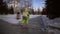 Cute child in a green jumpsuit walks through snow-covered park to school.