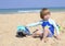 Cute child playing with toy car on sand beach. Happy sailor boy on sea coast.