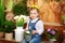 Cute child plays little gardener and plants flowers in pot on porch of the house. Little girl with potted flowers in garden. Happy