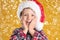 Cute child in Santa hat under snowfall on yellow background. Christmas celebration