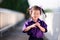 Cute child shows blushing expression when being photographed. Sweet smiley girl wearing purple dress.