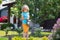 Cute child waters plants in backyard garden with watering can.