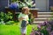 Cute child waters plants in backyard garden with watering can.