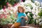 Cute child waters plants in backyard garden with watering can. Thumbs up.