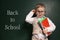 Cute child wearing glasses near chalkboard with phrase BACK TO SCHOOL