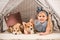 Cute child with welsh corgi dogs lying in wigwam and looking