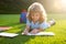 Cute childr boy with books with pencil writing on notebook outdoors. Summer camp. Kids learning and education concept