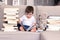 Cute clever little baby boy keen about reading book sitting on sofa with teddy bear toy and piles of books