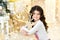 Cute close up portraite of curly girl with gold Christmas garlands magic lights and tree decorations hugs toy deer