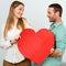 Cute couple holding big red heart sign.