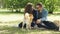 Cute couple man and woman are patting beautiful dog and talking sitting on lawn in the park. Modern lifestyle, domestic