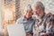 Cute couple of old people sitting on the sofa using laptop together shopping and surfing the net. Two mature people wearing