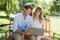 Cute couple sitting on park bench together looking at laptop