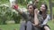 A cute couple of students taking selfie sitting on the grass in the park. The guy is in the foreground, the girl hugging