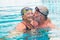 Cute couple of two seniors and pensioners at the pool swimming and having fun together - man kissing his wife - healthy and