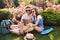 Cute couple of young people in sunglasses is chilling on grass on flowers background in park. Pretty girl with lon