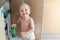 Cute curious caucasian baby boy open cupboard door in kitchen and exploring content. Funny toddler kid smiling and searching for