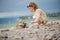 Cute curly child girl building stone tower on summer sea side