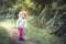 Cute curly child girl walking alone in forest on footpath among trees during summer holidays symbolizing happy carefree childhood