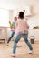Cute curly daughter mopping floor with mother and dancing