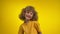 Cute curly girl with a charming toothless smile is smiling in a yellow studio