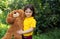 Cute curly girl in a yellow T-shirt smiles and hugs a large brown teddy teddy bear. greenery around