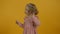 Cute curly kid in dress looking around on yellow background