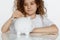 Cute curly little girl putting coin into big white piggy bank, over white background. Educational, saving money concept