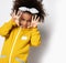 Cute curly mulatto african girl in warm yellow sports jumpsuit and hair bow frightening with hands and looking at camera