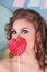 Cute curly woman hides her mouth behind lollipop