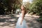 A cute curly woman in a white wedding dress with a wedding bouquet and wreath in her hair standing back to the camera in nature. C