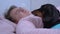 Cute dachshund lying down in owner embracing, male is sleeping in pink pajamas, pet in blue polka dot. Black and tan dog