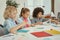 Cute diverse kids sitting together at the table while studying in elementary school classroom