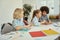 Cute diverse kids studying and drawing while sitting together at the table in elementary school classroom