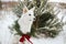 Cute dog in Christmas wreath sitting in snowy winter park. Adorable white swiss shepherd dog in stylish christmas wreath with pine