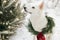 Cute dog in Christmas wreath sitting in snowy winter park. Adorable white swiss shepherd dog in stylish christmas wreath with pine