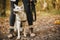 Cute dog sitting at owner legs in autumn woods. Traveling with pet, loyal companion. Adorable white swiss shepherd dog hiking with