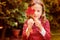 Cute dreamy child girl hiding behind red autumn leaf in the garden