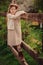 Cute dreamy kid girl in beige outfit climbing rustic wooden fence in spring garden