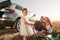 Cute dress on kid. Family have picnic at countryside near silver automobile at sunset